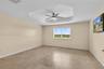 Interior room featuring a tray ceiling with a multi-blade ceiling fan and light fixture, stone-finish tile flooring, and a window with exterior landsc