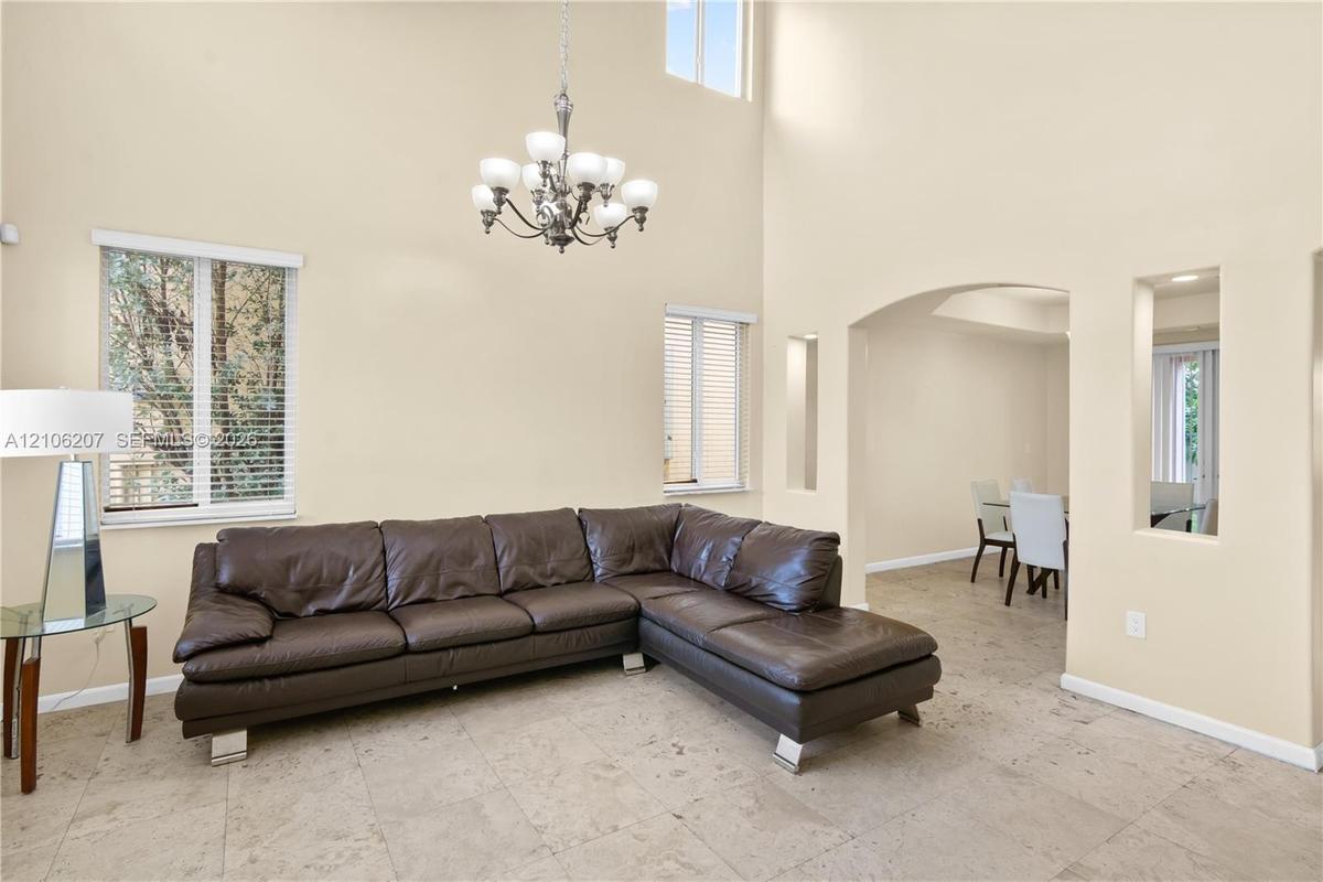 Vaulted ceilings featuring a multi-arm chandelier, neutral tile flooring, and arched architectural wall cutouts