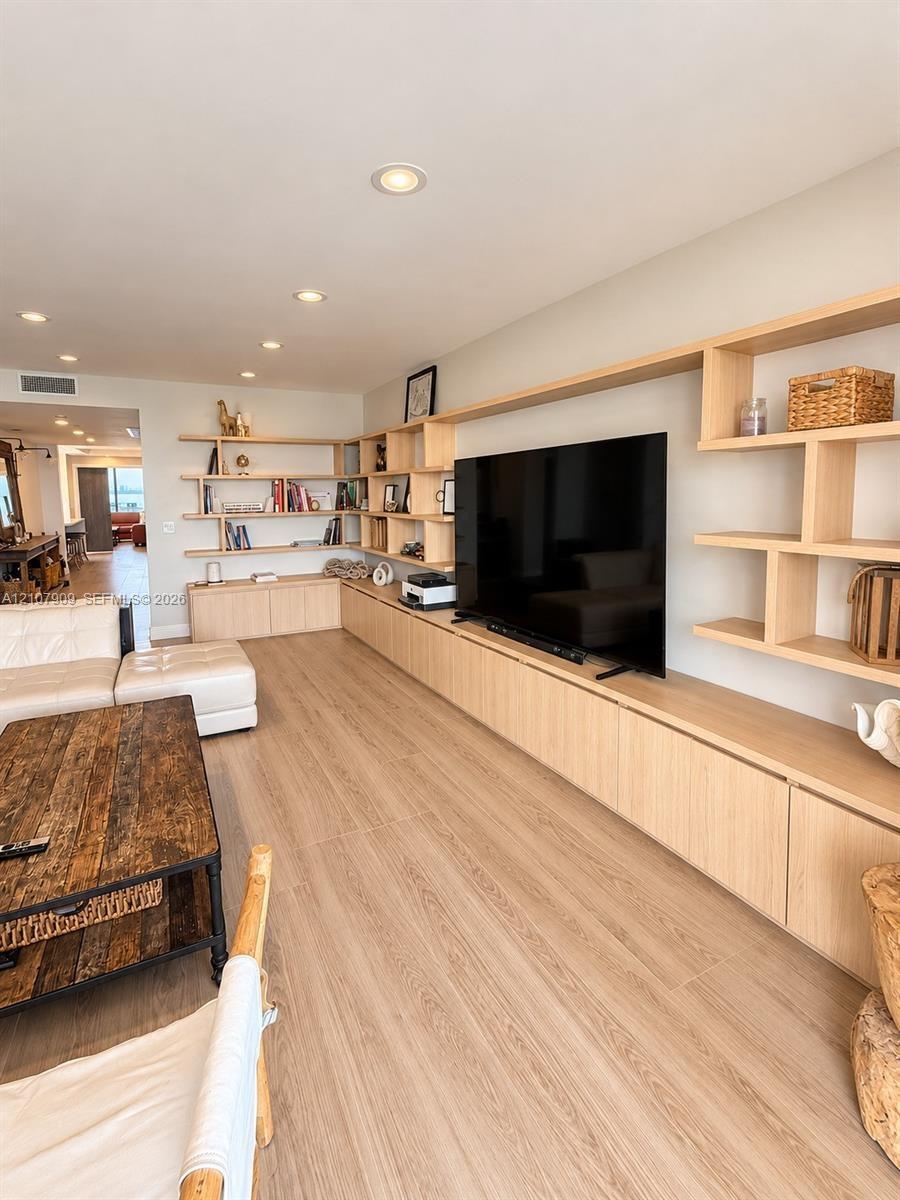 Custom light-tone cabinetry with extensive integrated shelving, recessed ceiling lighting, and continuous wood-finish flooring