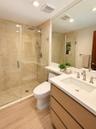 Bathroom featuring a frameless glass walk-in shower with stone wall tile, wood-finish cabinetry, quartz countertop with an integrated rectangular basi