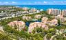 Aerial perspective of coastal residential structures featuring clay-tiled roofs, integrated water features, mature tropical landscaping, and proximity