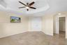 Tray ceiling featuring a central five-blade ceiling fan with integrated lighting, tile flooring, double-panel doors, and an arched entry to a walk-in 
