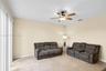 Neutral-toned living space featuring large-format tile flooring, a central ceiling fan with integrated lighting, and full-height sliding glass doors