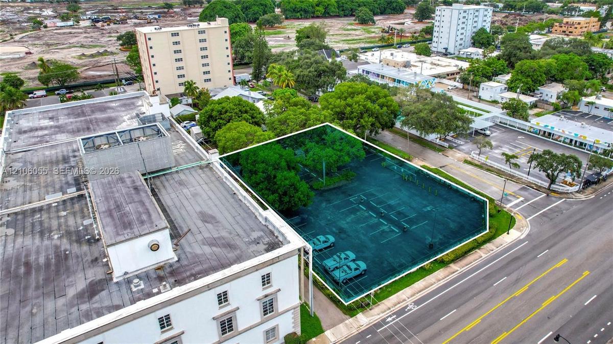 Paved parking lot featuring mature trees, a defined perimeter boundary, and street-level access