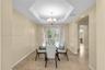 Tray ceiling with central chandelier, neutral wall tones, large-format stone-finish flooring, and glass doors with vertical blinds