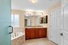 Bathroom featuring a double-sink vanity with wood cabinetry, stone-surround corner soaking tub, large wall-mounted mirror, and tile flooring