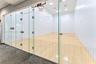Recreational court featuring frameless glass wall enclosures, high-contrast wood-finish flooring, recessed ceiling lighting, and a built-in basketball