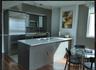 Kitchen featuring an island with a quartz countertop, stainless steel refrigerator, built-in microwave, track lighting, and wood-finish flooring