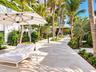Outdoor patio featuring natural stone paving, mature palm trees, tiered tropical landscaping, and a covered pavilion