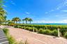 Brick-paver pathway featuring rope fencing, ornamental grasses, and mature palm trees