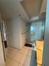 Walk-in glass enclosed shower with a polished metal faucet, white ceramic tile flooring, and a stone-surface vanity with an integrated sink
