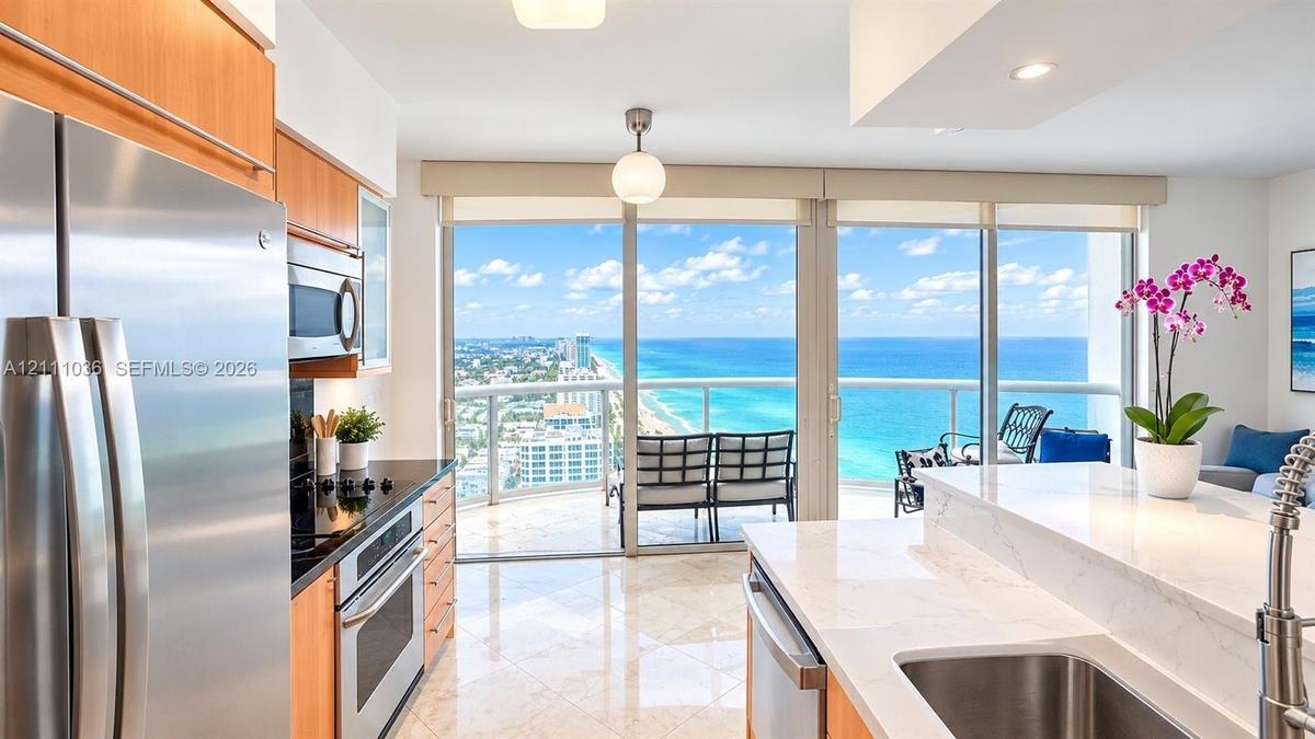 Kitchen featuring light-finish cabinetry, stone countertops, stainless steel appliances, polished tile flooring, and floor-to-ceiling glass doors open