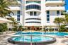 Multi-story exterior featuring curved balconies, floor-to-ceiling windows, a circular spa with tiled surround, a sprawling swimming pool, and stone pa