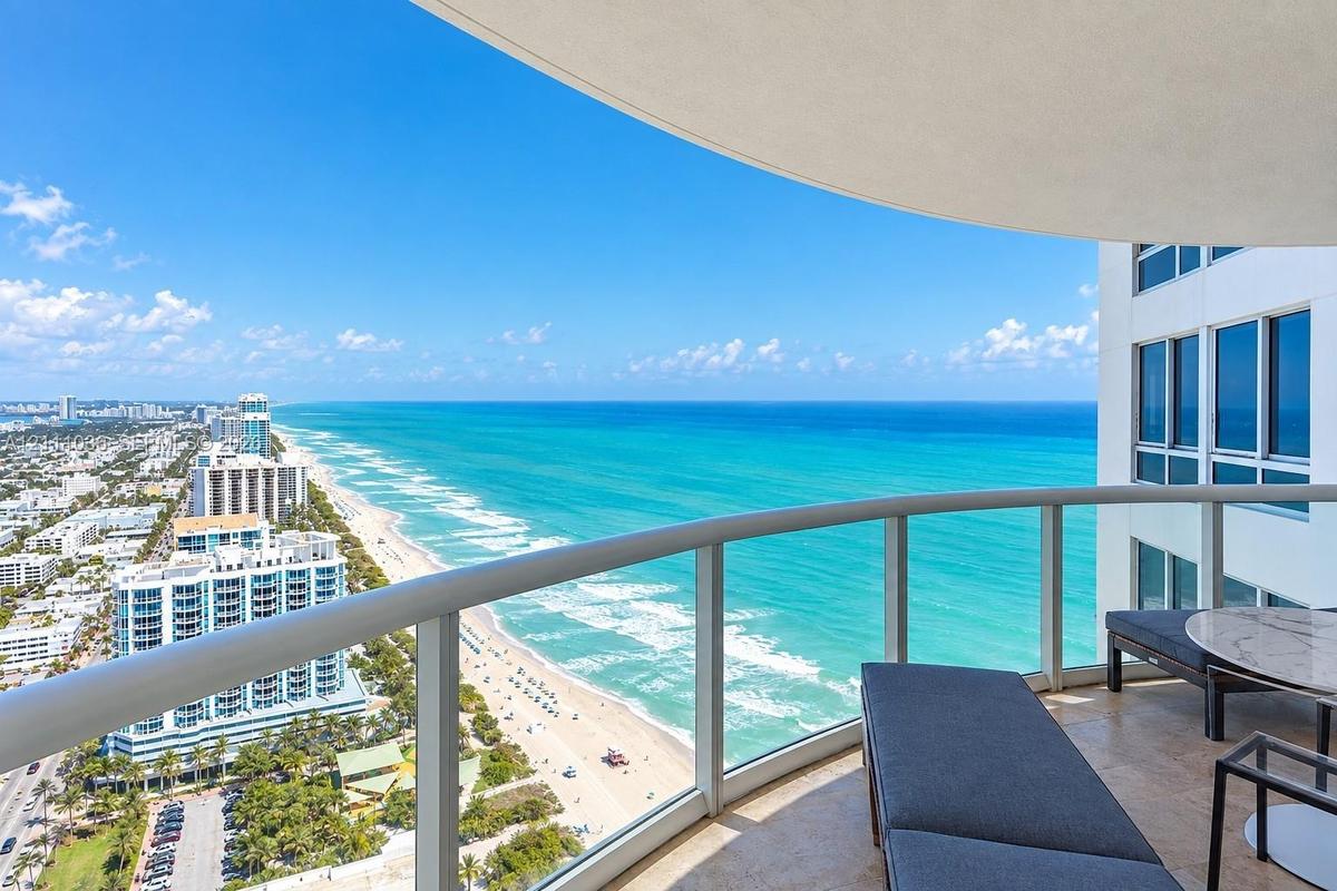 Curved covered balcony with stone flooring and glass panel railing overlooking the coastline