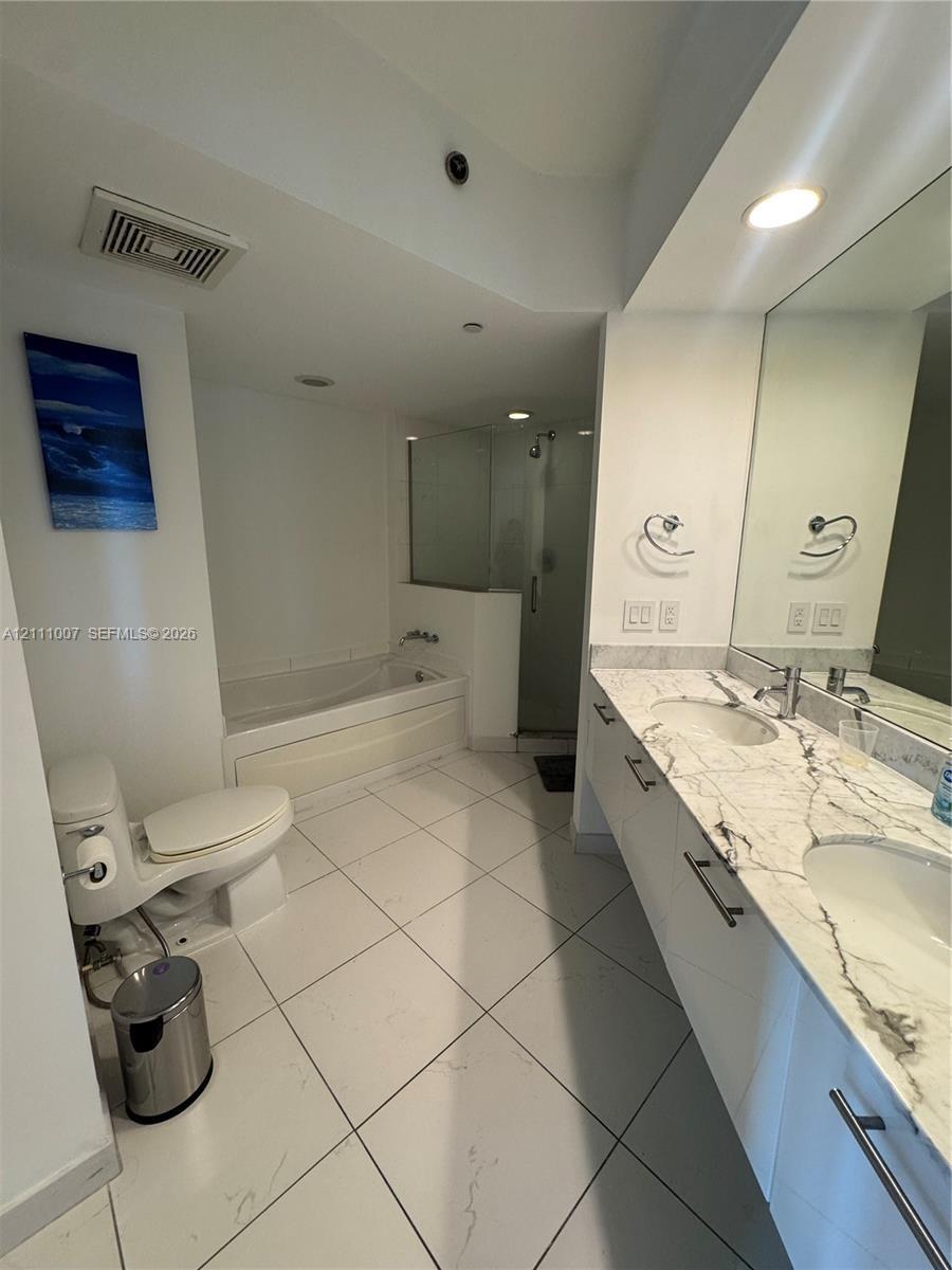 Double vanity featuring white cabinetry, stone-finish countertops with integrated dual sinks, and matte-finish hardware, paired with a deep soaking tu