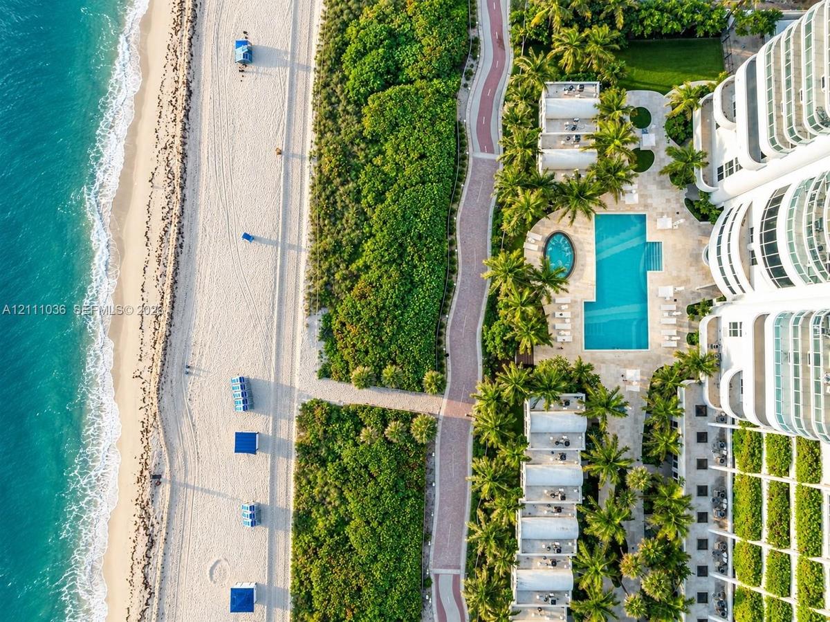 Oceanfront property featuring direct beach access, a rectangular swimming pool, a separate circular spa, paved pedestrian pathways, and lush tropical 