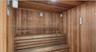 Sauna featuring wood paneling, multi-level slatted wooden benches, and wall-mounted lighting fixtures