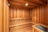 Sauna featuring tongue-and-groove wood paneling, multi-level built-in bench seating, recessed ceiling lighting, and a stone-filled heating unit with a