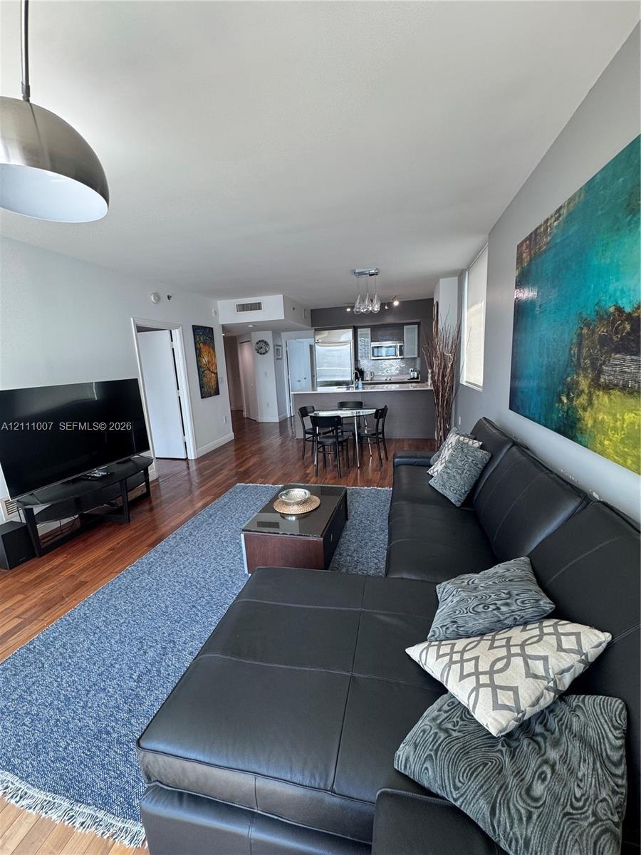 Open-concept living space featuring wood-finish flooring, recessed lighting, and a kitchen equipped with a breakfast bar and stainless steel appliance