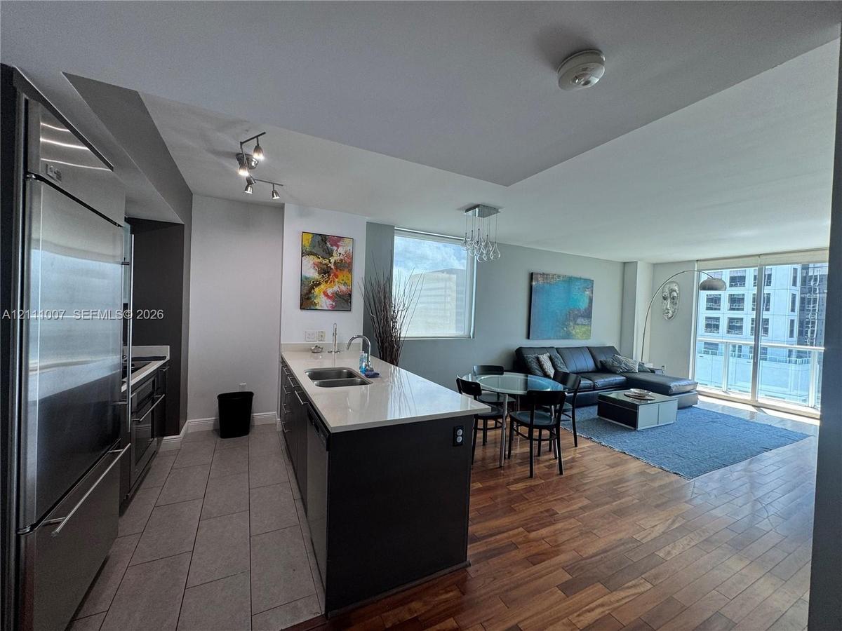 Open-concept kitchen featuring an island with a light-toned solid surface countertop, stainless steel refrigerator, tile flooring, and wood-finish flo
