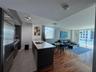 Open-concept kitchen featuring an island with a light-toned solid surface countertop, stainless steel refrigerator, tile flooring, and wood-finish flo