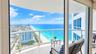 Covered wrap-around balcony featuring glass panel railings, stone flooring, and expansive coastal and urban scenery