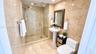 Full-height natural stone wall tiling, walk-in glass-enclosed shower, pedestal sink, and polished chrome fixtures