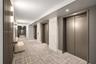 Elevator lobby featuring metallic-finish elevator doors, floor-to-ceiling stone-clad surround, wood-slat accent wall, and recessed lighting