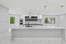 Kitchen featuring a large waterfall-edge island with stone-finish countertops, matte black faucet, integrated stainless steel double oven, two-tone ca