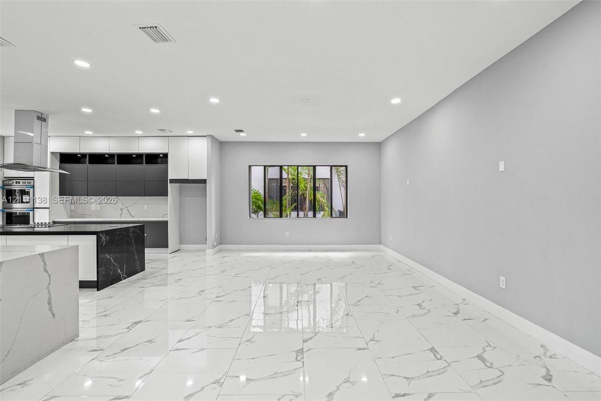Open-concept interior featuring large-format polished stone-finish flooring, two-tone cabinetry with contrasting stone-finish countertops, stainless s