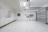 Garage featuring expansive stone-finish flooring, extensive white built-in cabinetry, overhead task lighting, and an automated sectional door