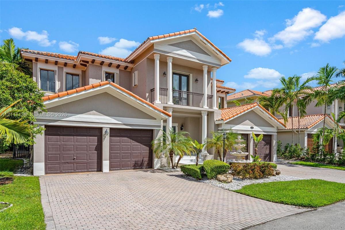 Two-story stucco exterior featuring a tiled roof, multi-bay garage, covered entryway with classical columns, second-level balcony, and decorative ston