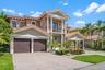 Two-story stucco exterior featuring a tiled roof, multi-bay garage, covered entryway with classical columns, second-level balcony, and decorative ston