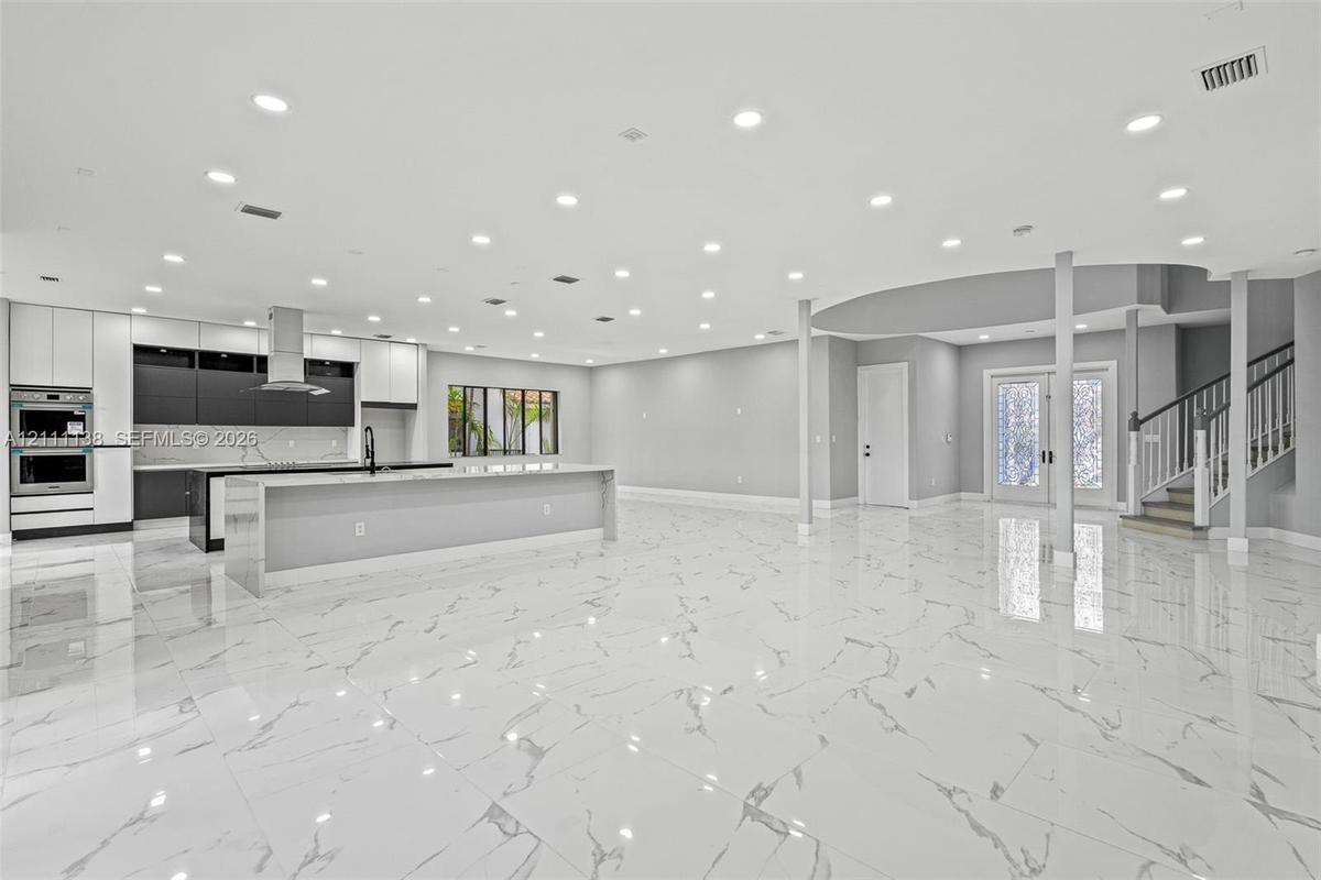 Open-concept interior featuring large-format tile flooring, recessed lighting, a modern kitchen with a dual-tone cabinetry finish, a central island, a