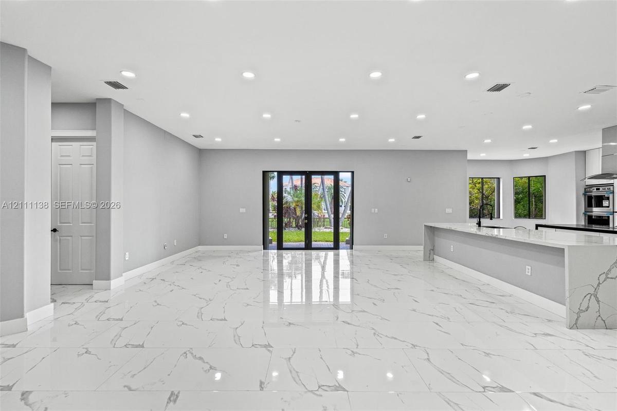 Open-concept interior featuring large-format polished stone flooring, recessed ceiling lighting, a waterfall-edge kitchen island, and double glass-pan