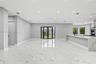Open-concept interior featuring large-format polished stone flooring, recessed ceiling lighting, a waterfall-edge kitchen island, and double glass-pan
