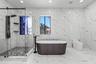 Full-height, large-format stone-patterned wall tile, freestanding soaking tub with floor-mounted matte black faucet, glass-enclosed walk-in shower wit