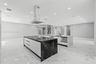 Dual kitchen islands featuring stone-finish waterfall countertops, flat-panel cabinetry, a stainless steel chimney-style range hood, and porcelain til