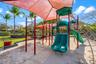 Outdoor recreational area featuring a multi-component play structure with dual slides, suspended shade canopy, rubberized mulch surfacing, and perimet