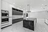 Kitchen featuring flat-panel cabinetry, a waterfall-edge island with an integrated cooktop, quartz countertops with a veined pattern, a stainless stee