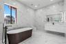 Bathroom featuring floor-to-ceiling large-format tile with stone-pattern finish, wall-mounted floating vanity, freestanding soaking tub with matte bla
