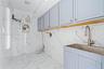 Utility area featuring floor-to-ceiling large-format stone-finish wall tile, light blue shaker-style cabinetry, a stainless steel basin sink, and a go