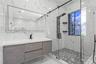 Floating vanity with integrated sink, floor-to-ceiling large-format tile walls, walk-in shower with glass enclosure, multi-head shower panel, and hexa