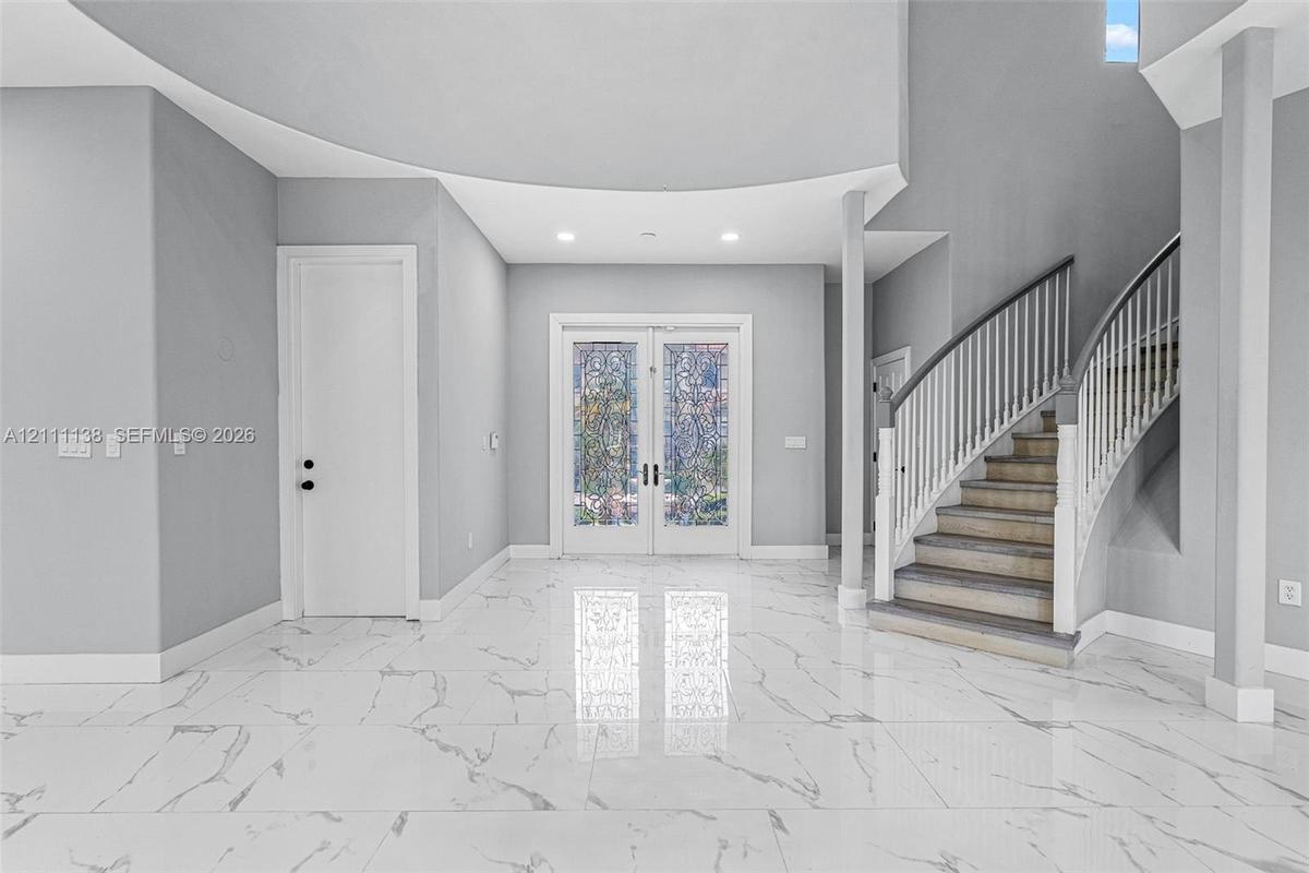 Foyer featuring large-format veined tile flooring, a curved staircase with white spindles, high ceilings with recessed lighting, and double-entry door