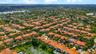 Aerial perspective highlighting a residential property featuring a tile roof, paved driveway, and proximity to neighborhood lakes and tropical landsca