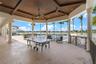 Covered outdoor patio featuring a wood-paneled coffered ceiling, stone-finished flooring, decorative columns, and a metal railing overlooking a pool a