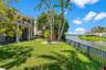 Waterfront backyard featuring a manicured lawn, metal perimeter fencing, mature palm trees, and a two-story exterior with a curved balcony