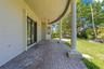 Covered curved patio featuring brick pavers, classical columns, and a ceiling-mounted fan