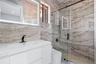Modern vanity with a rectangular integrated sink, wall-mounted backlit mirror, walk-in shower with sliding glass door, and large-format natural stone 