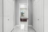 Hallway featuring white panel doors with matte black hardware and polished stone-finish floor tile with veining, leading into a space with matching st